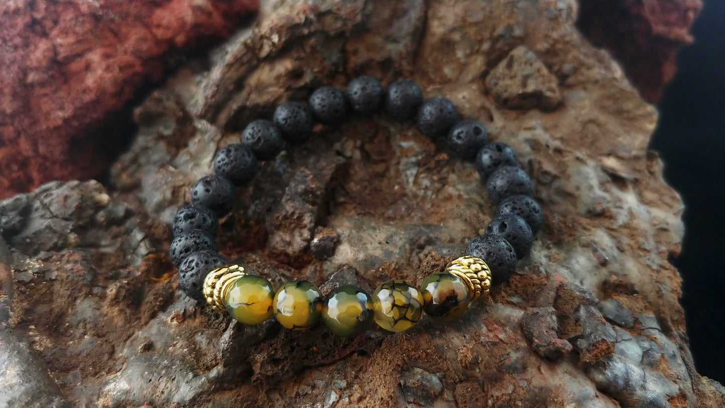 Bracelet sitting on a dark brown rock. The bracelet is mostly made with lava rock beads 8mm in size. In the center there are 5 green colored beads called dragon vein beads. On each side there are golden colored spacers.