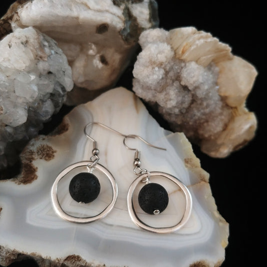 Silver circle hearrings with silver rings that have a dangling dark black lava beads in the center. Earring are displayed on an icelandic opal stone display.