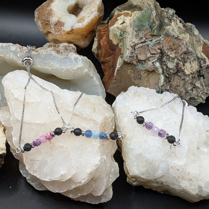 Three silver adjustable bracelets displayed on white crystal clusters, set against a dark background with natural rock formations.