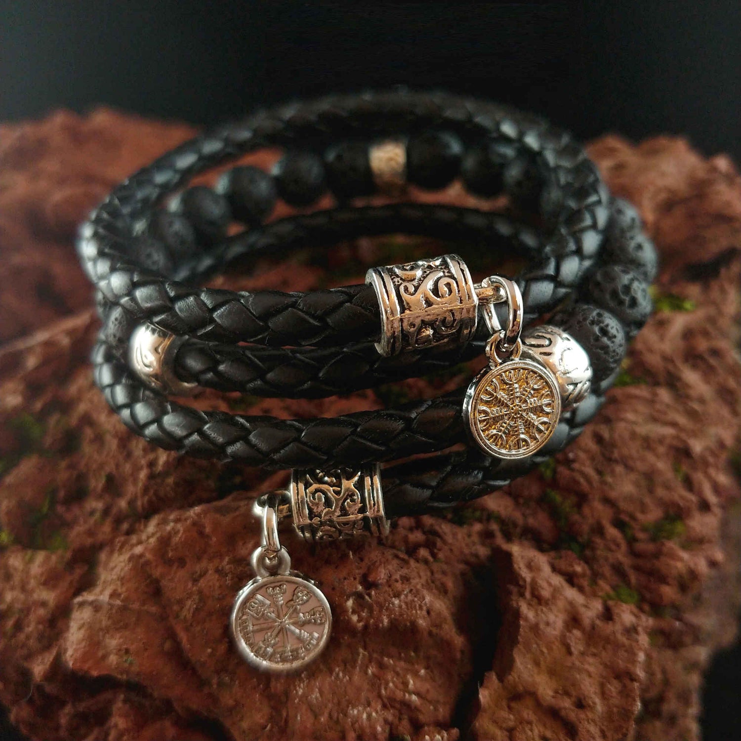 dark black leather bracelet with Vegvisir and Ægishjalmur silver charms. The bracelet sits on top of a red lava rock.