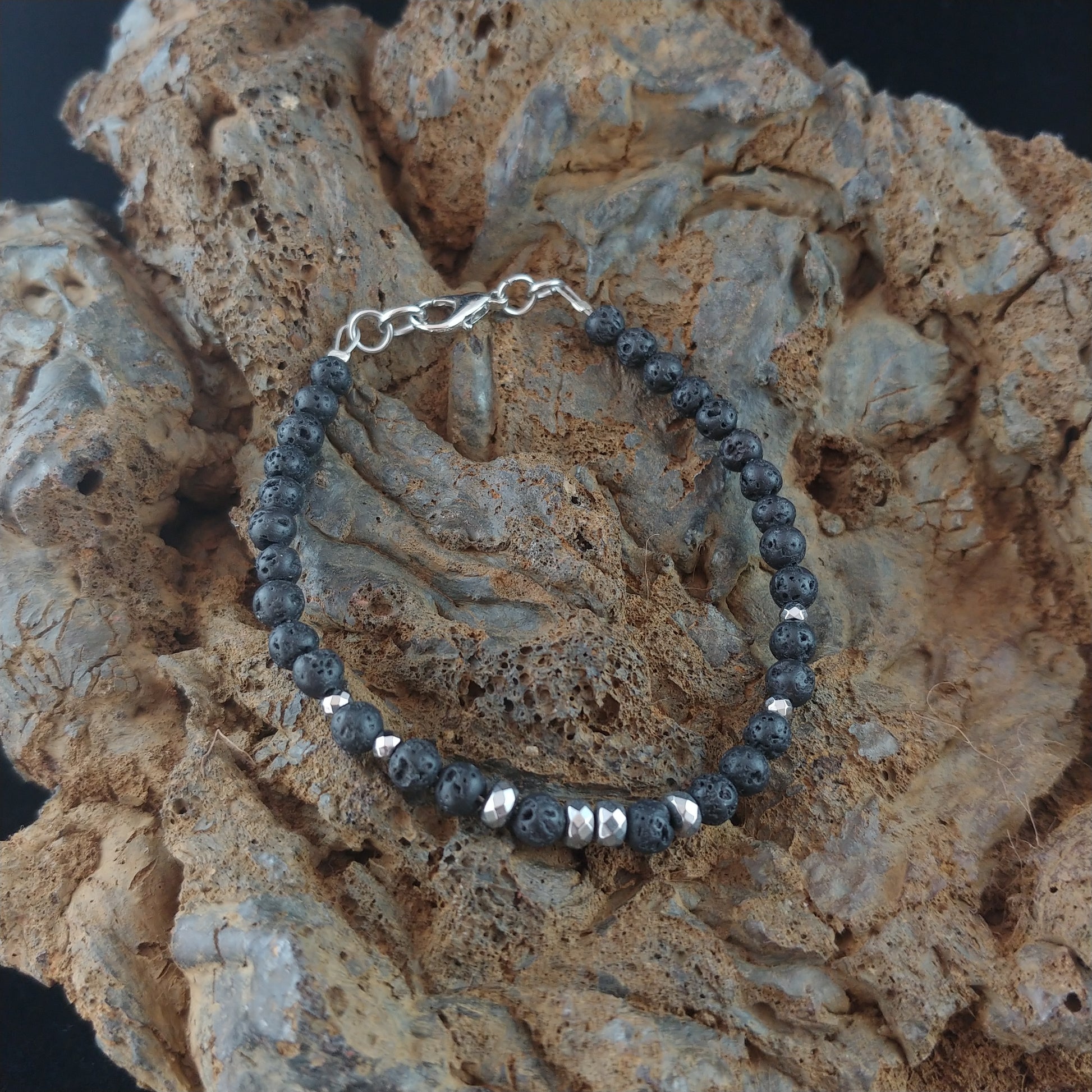 Lava beads bracelet with small 4mm lava beads. The bracelet has a chain and lobster claw clasp. The bracelets sits on a dark magma rock display