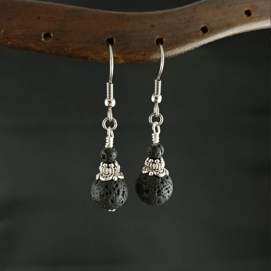 Earrings being displayed on an old wood stand. The earrings have large lava beads with silver caps with avant-garde symbols. Above that are 4mm small lava stones.