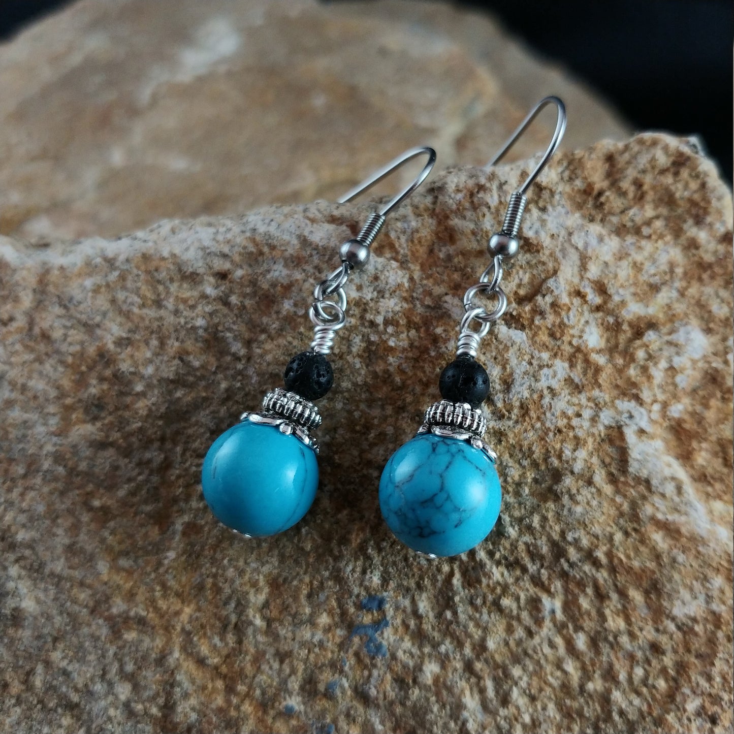 earrings with a small lava bead and on the bottom larger 10mm Blue Turquoise beads. between the stones there is a silver colored cap.