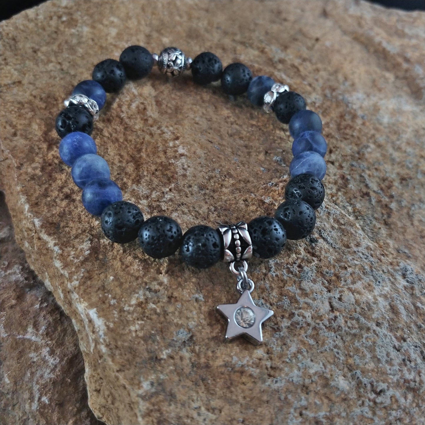 Bracelet with dark blue beads and black lava beads sitting on top of a rock display. The bracelet has a silver colored star centerpiece.