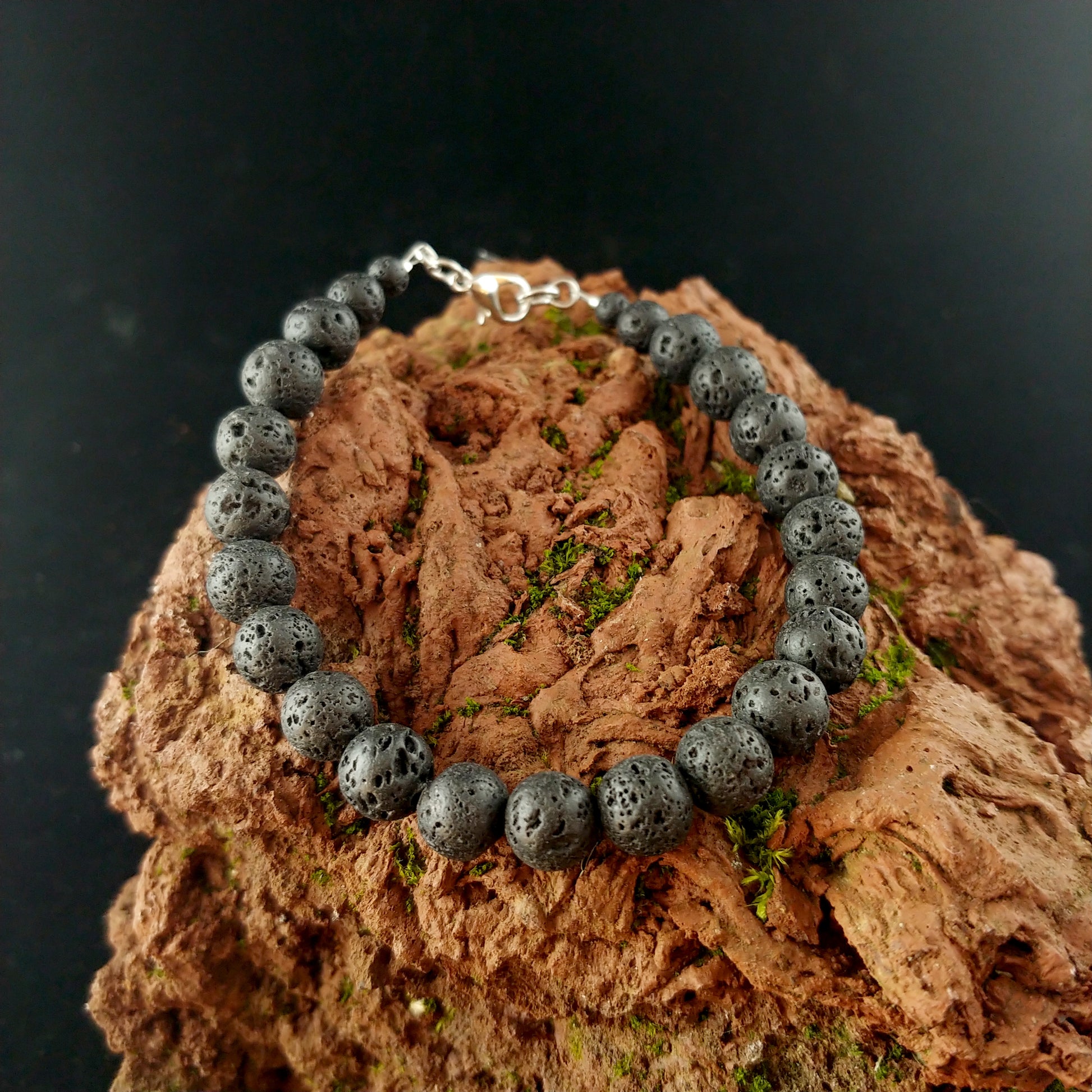 Plain lava rock bracelet with dark black round lava stones. The bracelet has a lobster claw clasp. The bracelet sits on a red magma lava rock.